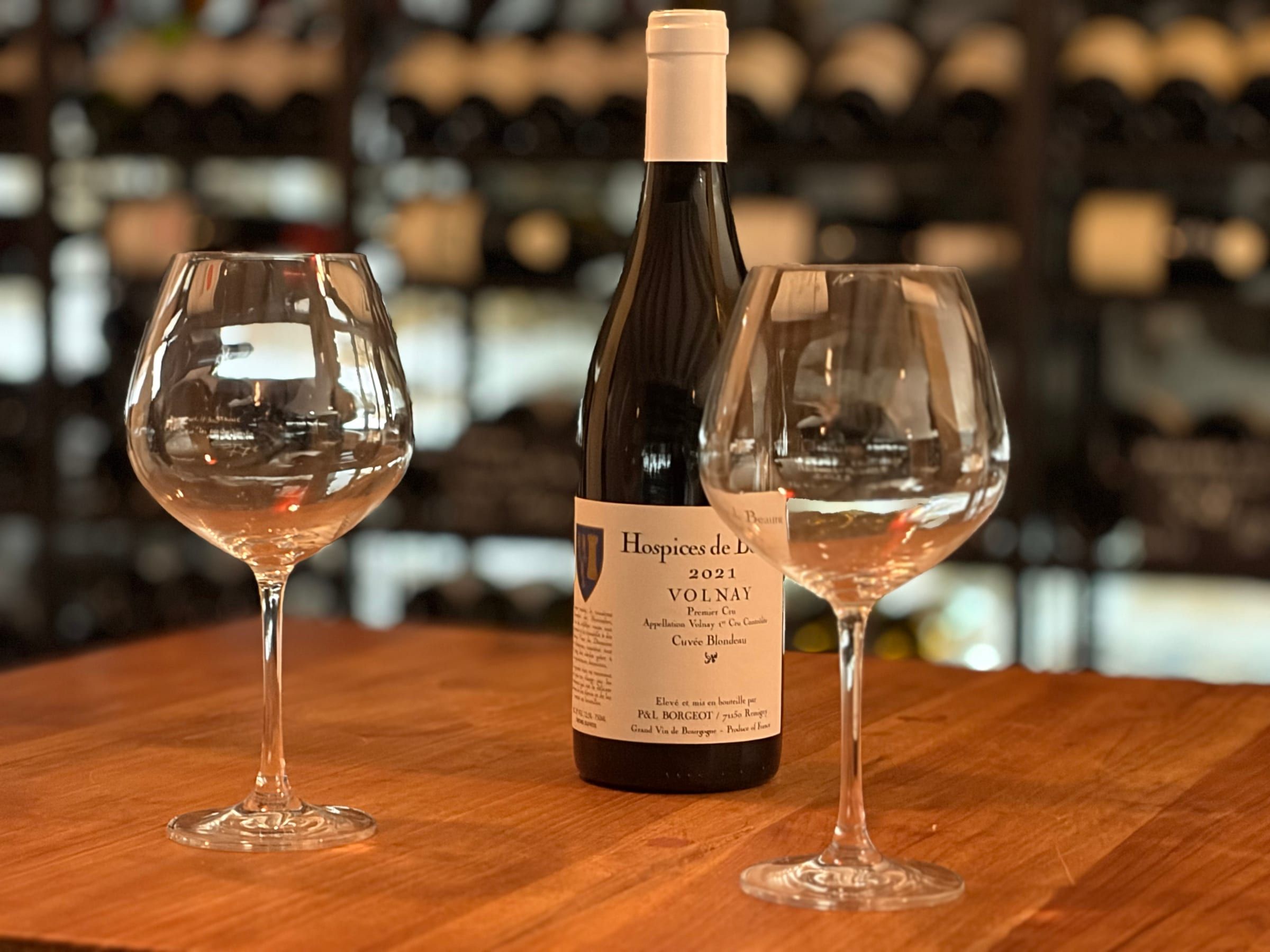 Deux verres à vin et bouteille de Volnay Premier Cru Hospices de Beaune sur table en bois