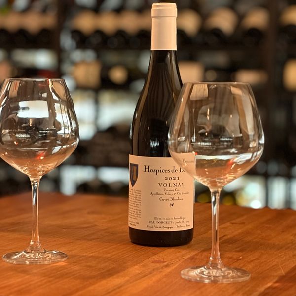 Deux verres à vin et bouteille de Volnay Premier Cru Hospices de Beaune sur table en bois