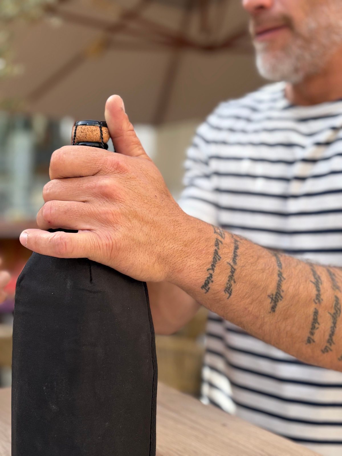 Ben, le caviste de L'Oenothèque en marinière, avant-bras tatoué, la main sur une bouteille qu'il s'apprête à servir