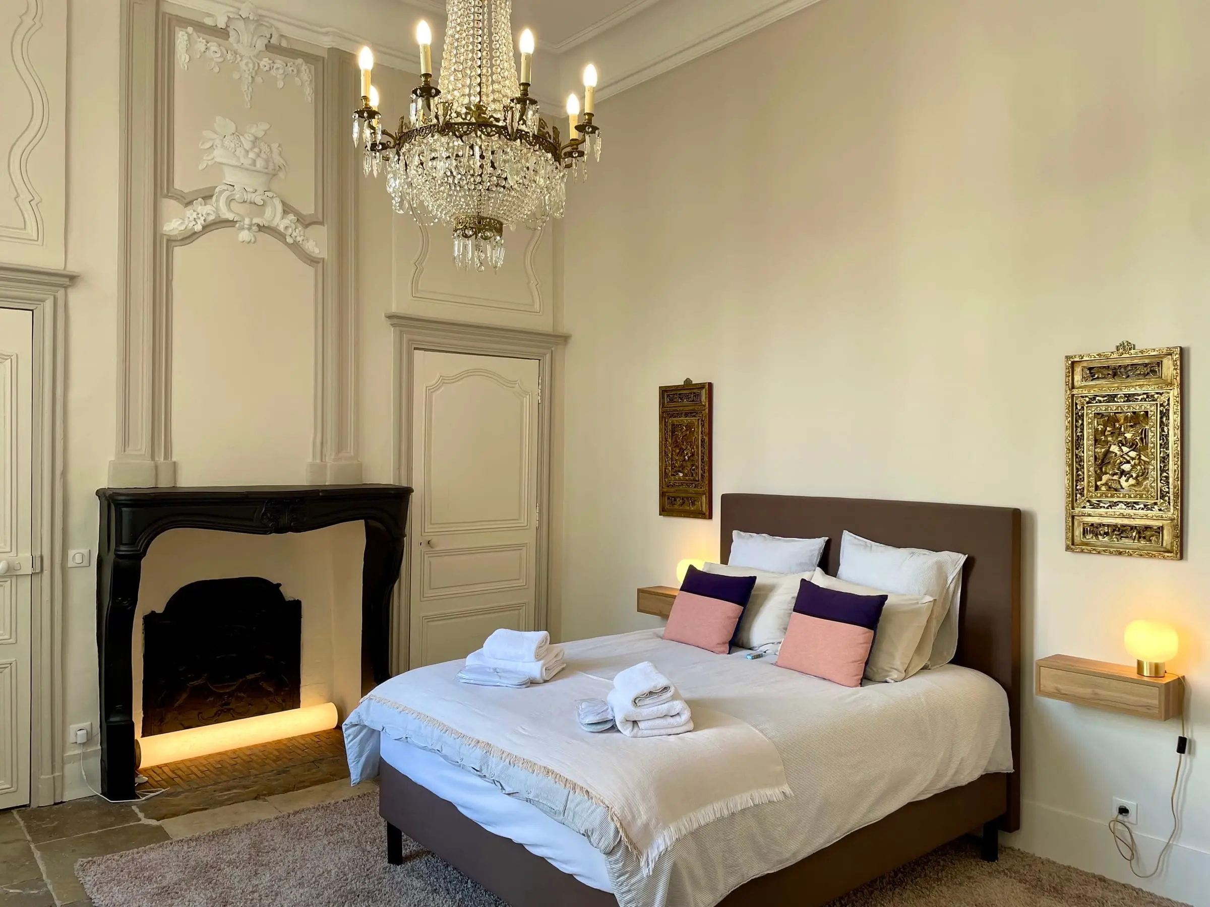 Chambre avec lustre en cristal, cheminée noire et coussins rose et violet