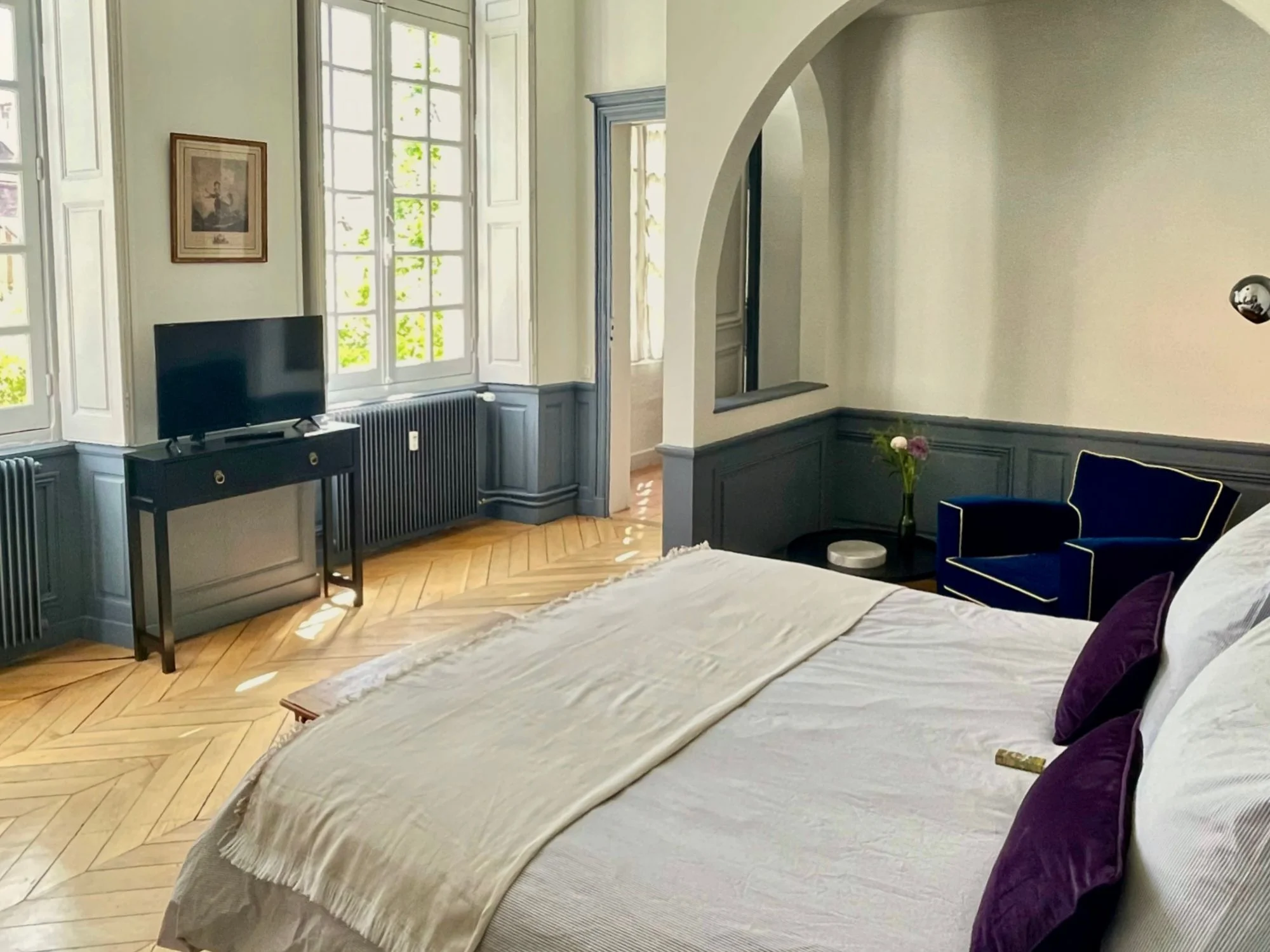 Chambre spacieuse avec parquet en chevrons, boiseries bleu gris et fauteuil en velours