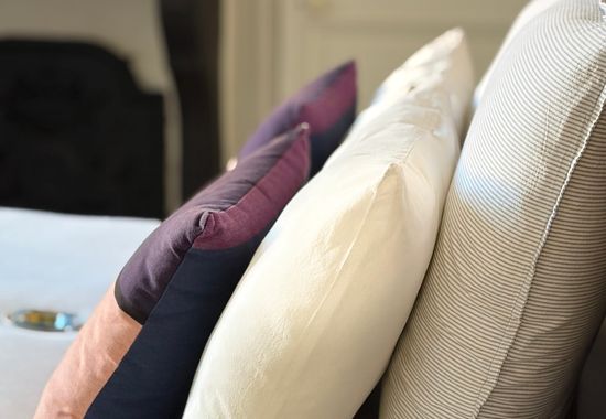Détail de coussins aubergine, ivoire et rayures fines posés sur le lit
