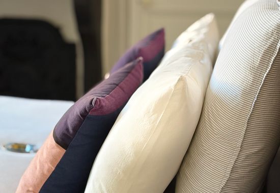 Détail de coussins aubergine, ivoire et rayures fines posés sur le lit