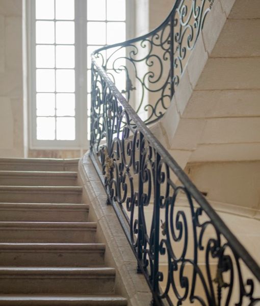 Escalier en pierre et rambardes en fer forgé ouvragé baignés de lumière naturelle
