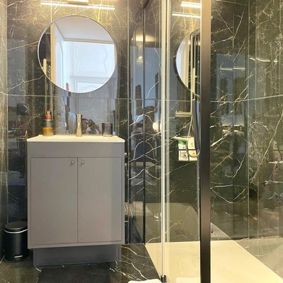Salle de bain en marbre noir avec miroir rond et douche vitrée